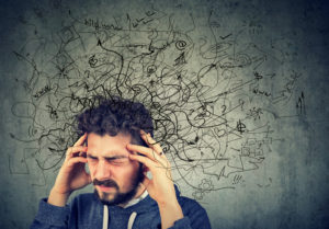 Young man holding his forehead while squiggles of worry and anxiety surround his head